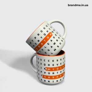 Ігровий дизайн на чашках — стильне брендування зі словами, які надихають Дві білі чашки з чорним текстовим принтом та помаранчевими виділеннями слів